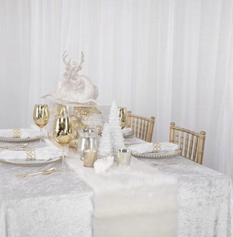 Winter white holiday tablescape with crushed velvet linen, gold chiavari chairs, and white reindeer centerpiece